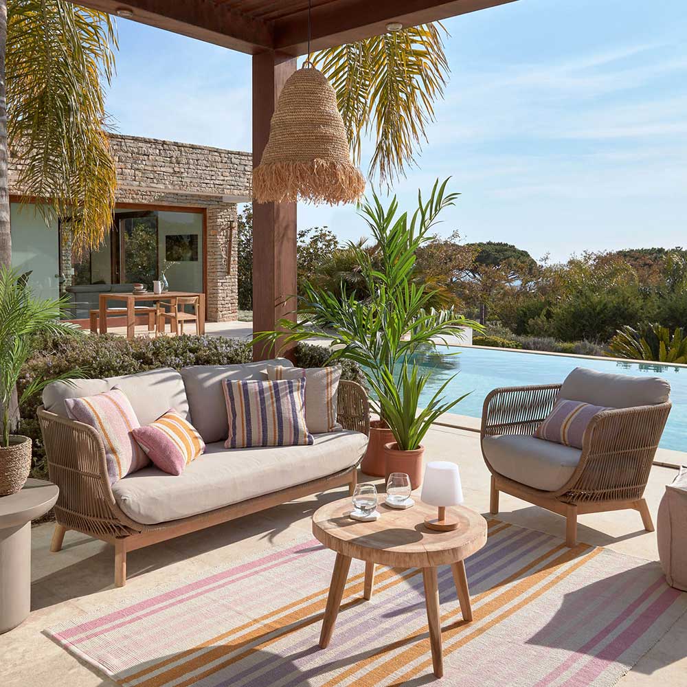 Outdoor Sofa aus Kordelgeflecht mit hellen Polstern auf einer sonnigen Terrasse – Calivias