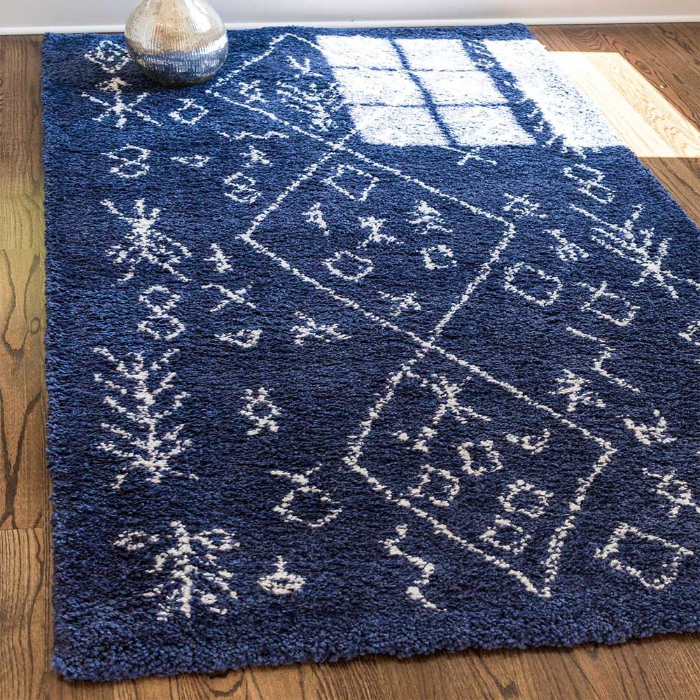 Blauer Shaggy Teppich mit weißem Ethno Design auf dunklem Holzfußboden – Avior