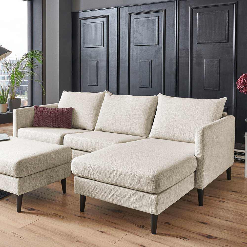 Cremefarbenes L-Sofa in modernem Wohnambiente mit schwarzen Füßen – Bentema