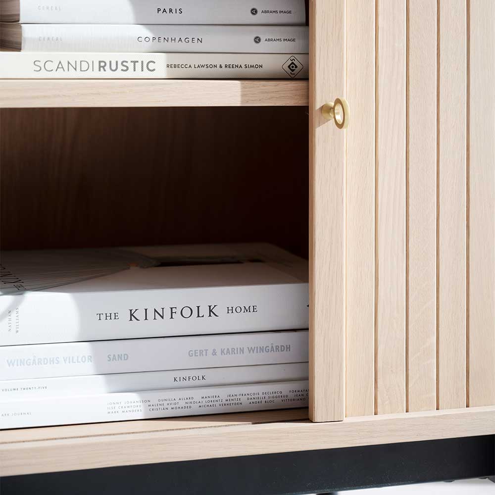 Helle Holzkommode mit geöffneter Lamellentür, goldenem Griff und Büchern im Fach – Troyes