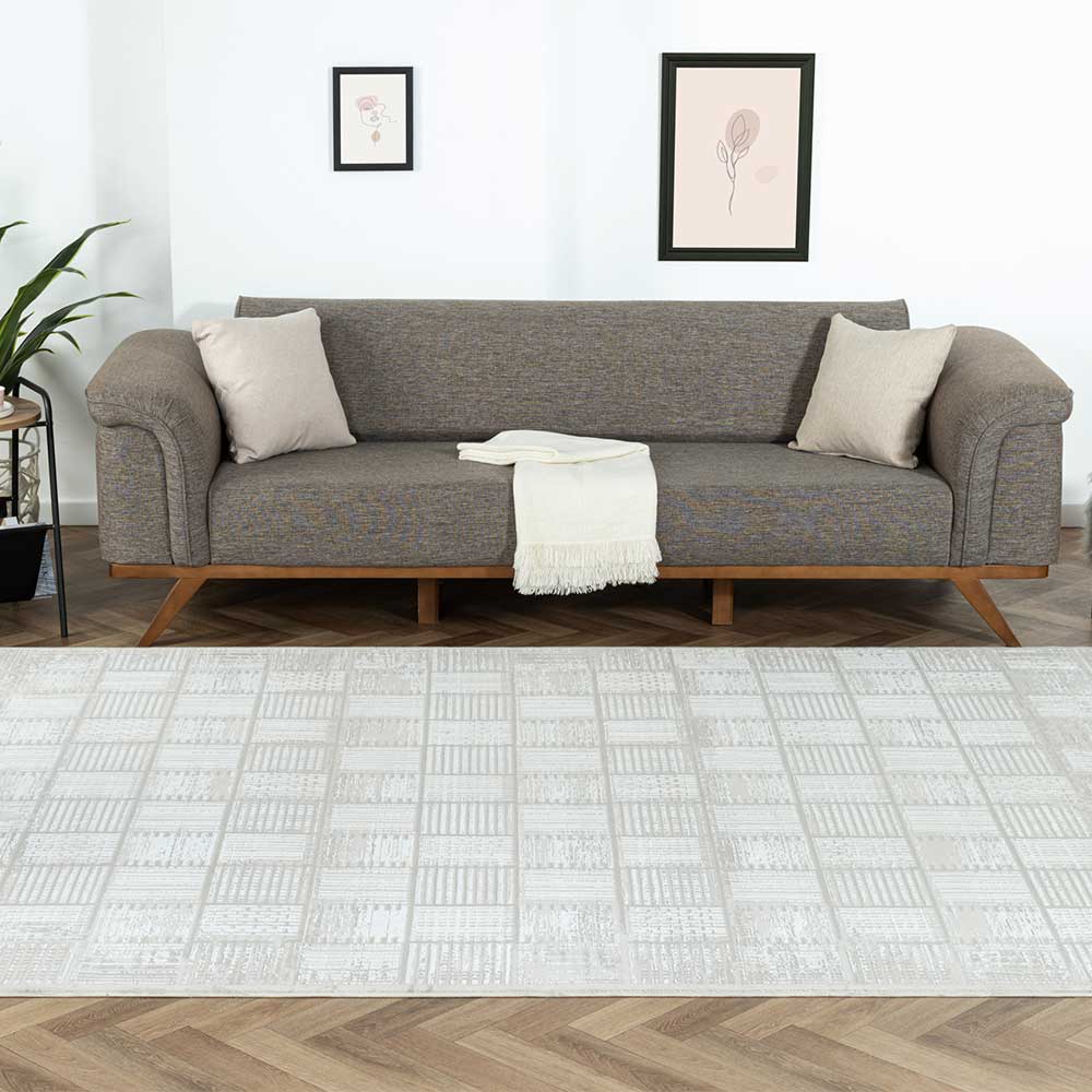 Heller Teppich mit geometrischem Kachelmuster vor einem Sofa im Wohnbereich – Pahat