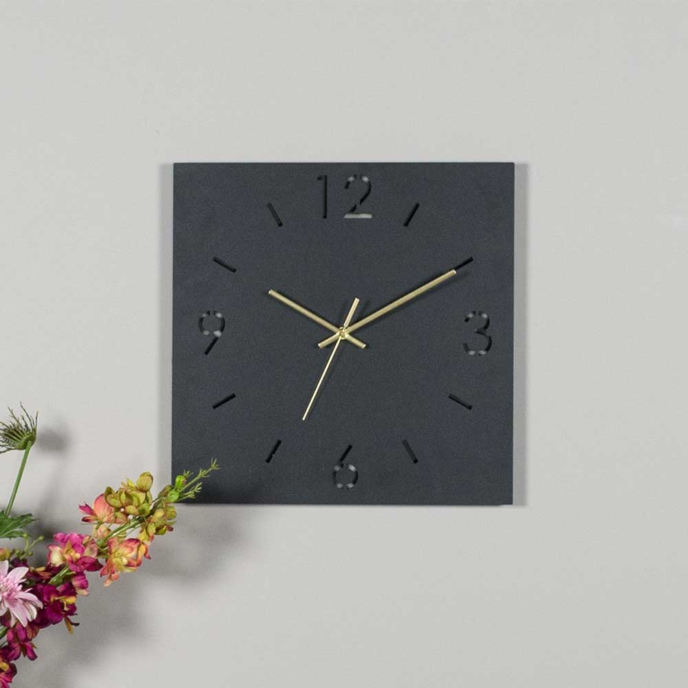 Moderne quadratische Wanduhr in Dunkelgrau mit goldfarbenen Zeigern an einer hellgrauen Wand   – Britain