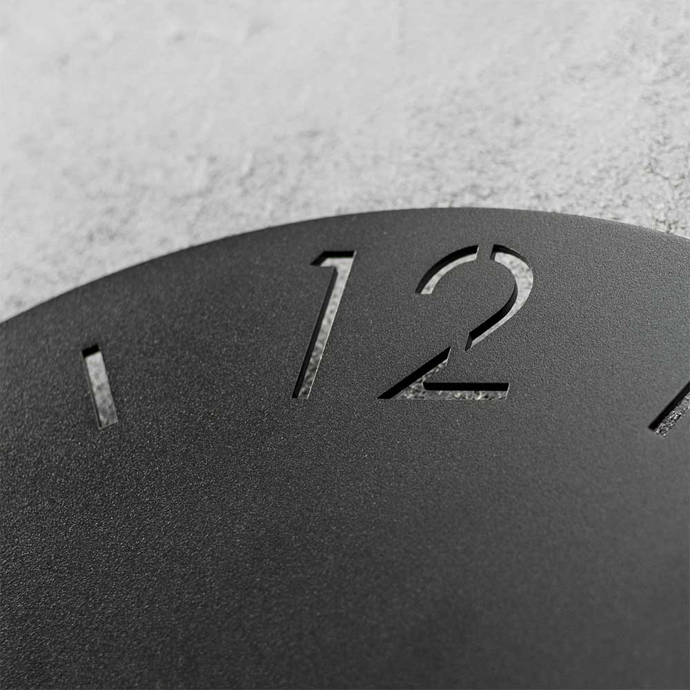 Detailaufnahme der mattschwarzen runden Uhr mit ausgeschnittener Ziffer 12 – Santorina